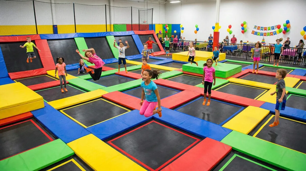 Groupe d'enfants joyeux sautant sur des trampolines colorés dans un parc intérieur pour un anniversaire.