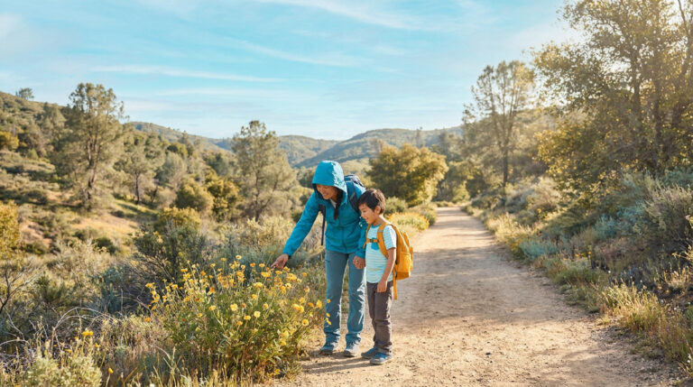 Une mère et son jeune fils en randonnée, observant des fleurs jaunes sur un sentier en pleine nature.