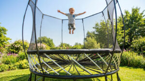 Un petit garçon joyeux saute en l'air sur un trampoline de jardin moderne sans ressorts dans un parc ensoleillé.