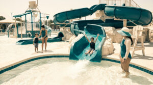 Mère et enfants s'amusent dans un parc aquatique avec des toboggans et une structure de jeux.
