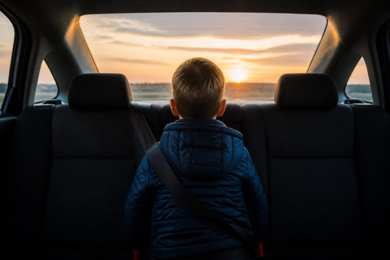 Un jeune garçon assis à l'arrière d'une voiture regarde le soleil couchant à travers la lunette arrière.