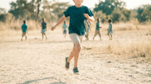 Un jeune garçon court joyeusement sur un chemin de terre avec d'autres enfants en arrière-plan.