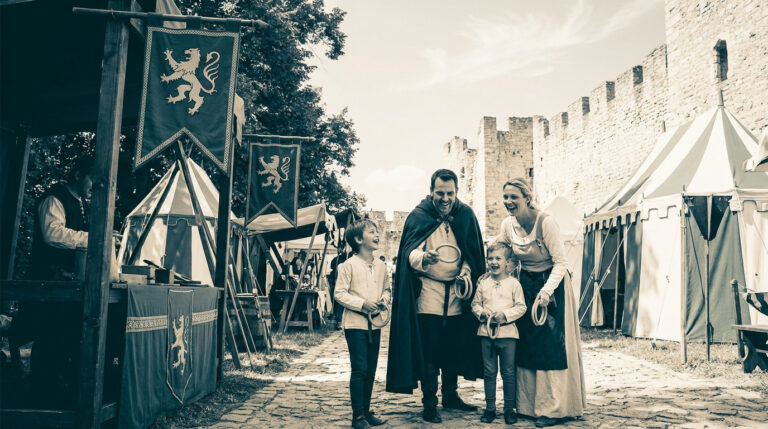 Une famille en costumes médiévaux joue à un jeu d'anneaux devant les tentes d'un campement historique.