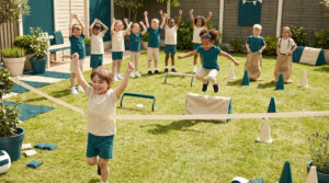 Un jeune garçon franchit joyeusement la ligne d'arrivée d'une course, suivi par d'autres enfants jouant dans un jardin.