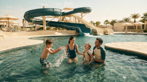 Famille joyeuse s'amusant dans la piscine d'un parc aquatique avec des toboggans en arrière-plan.
