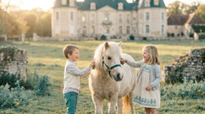 Un petit garçon et une fillette brossent un poney blanc devant un château à Maisons-Laffitte lors d'un anniversaire.