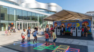 Des enfants jouent à une marelle numérique lumineuse devant le bâtiment de la Philharmonie des enfants à Paris.
