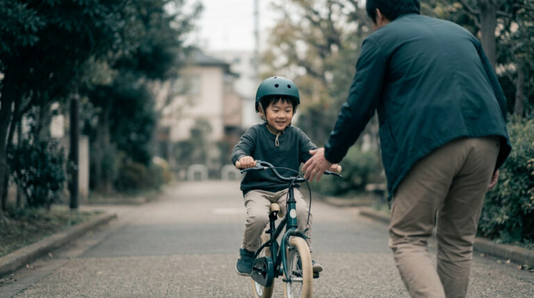Un jeune enfant avec un casque apprend à faire du vélo sous la supervision bienveillante de son père dans une rue.