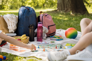 Enfants jouant à un jeu de société sur une couverture de pique-nique avec sacs, gourdes et ballon.