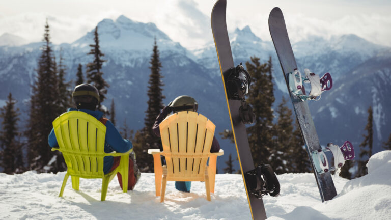 Snowboardeurs au repos dans des chaises colorées face aux sommets enneigés, vacances de février en station