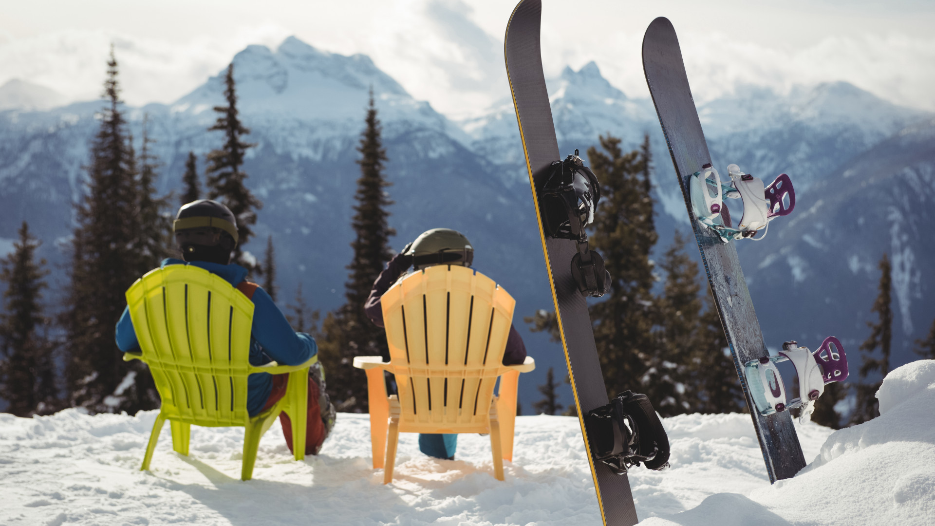 Snowboardeurs au repos dans des chaises colorées face aux sommets enneigés, vacances de février en station